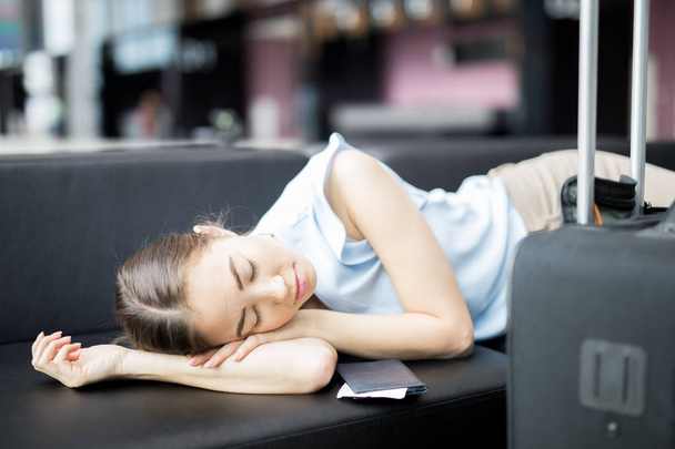 Havaalanının dinlenme odasında siyah deri koltukta kestirip duran genç ve yorgun bir kadın. - Fotoğraf, Görsel