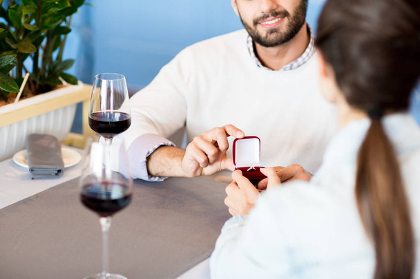 Hombre amoroso mostrando anillo de diamantes de mujer joven en caja de terciopelo mientras hace su propuesta en el restaurante
 - Foto, Imagen