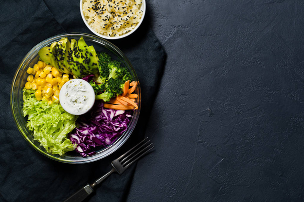 Buddha bowl, healthy and balanced food. Ingredients broccoli, corn, carrots, couscous, lettuce, cabbage, sauce. Black background, top view, space for text - Fotó, kép