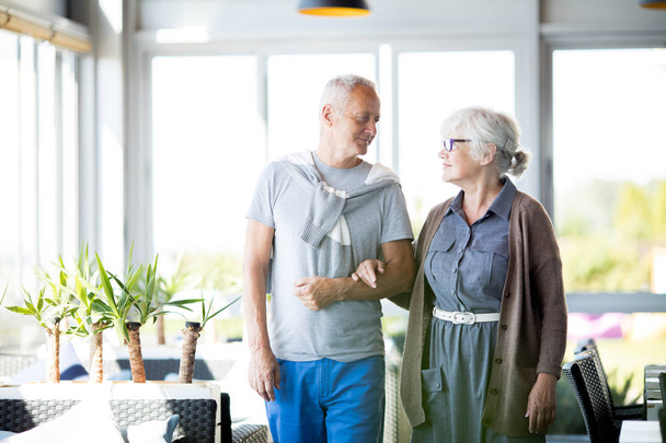 Portrét milující starší pár pózuje ruku v ruce a při pohledu na sebe něžně stoje v kavárně - Fotografie, Obrázek