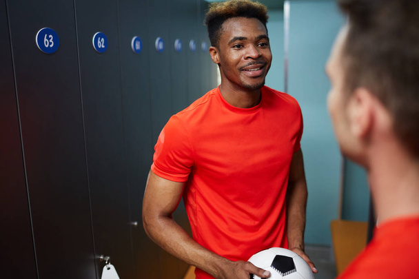 African-american guy in football uniform looking at his mate during their conversation in changing-room - Photo, Image