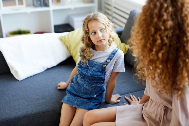 Nettes kleines Mädchen in Freizeitkleidung sitzt auf dem Sofa neben ihrer Mutter und hört zu, was sie sagt - Foto, Bild