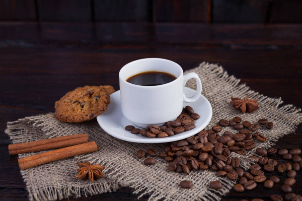 近くのコーヒー穀物や暗いヴィンテージ背景にリネン生地の上にビスケットとコーヒーの白いカップ - 写真・画像