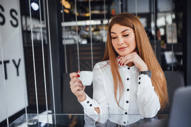 Businesswoman in white blouse sitting at table and looking down at cup of coffee  - Fotografie, Obrázek