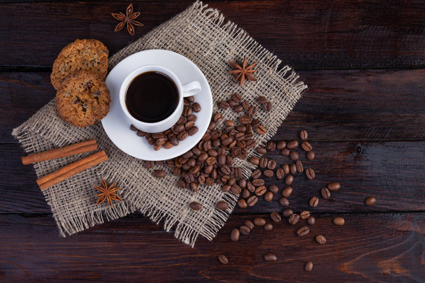 近くのコーヒー穀物や暗いヴィンテージ背景にリネン生地の上にビスケットとコーヒーの白いカップ - 写真・画像