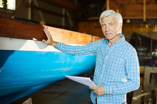 Уверенный в себе опытный судостроительный инженер с бумагой, стоящей у недавно построенного судна и смотрящий в камеру
 - Фото, изображение