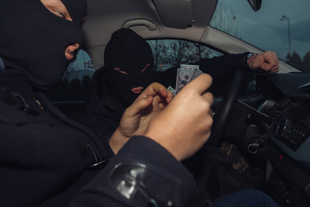 Dos ladrones enmascarados contando el dinero que ganaron mientras estaban sentados
 - Foto, Imagen