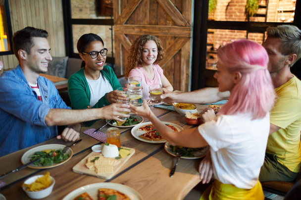 Ευτυχισμένοι νέοι φίλοι τοστ με ποτήρια λεμονάδα απολαμβάνοντας το δείπνο στο καφέ - Φωτογραφία, εικόνα