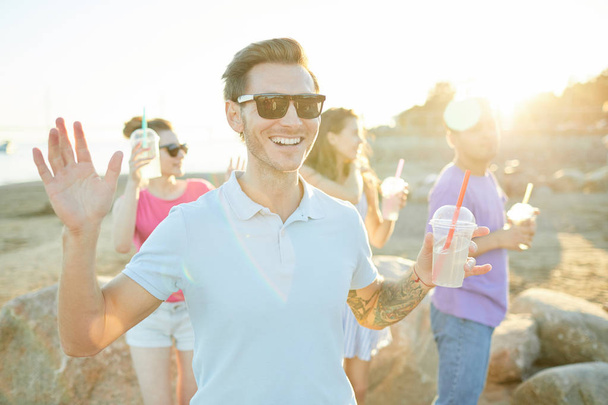 Smiling guy with glass of drink having fun and dancing outdoors with his frirnds on background - Fotoğraf, Görsel