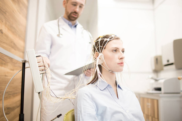 Paciente joven con electrodo en la cabeza y su médico controlando el procedimiento
 - Foto, imagen