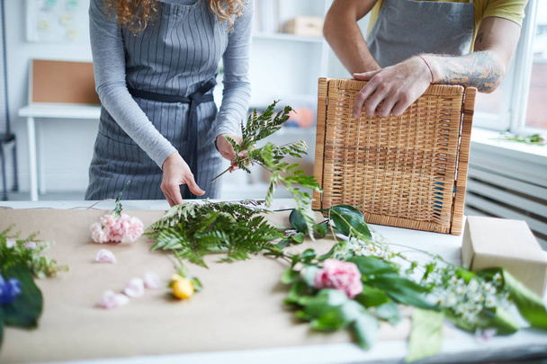 junge Floristin legt Farnblätter in einen Strauß, während ihre Kollegin in der Nähe steht - Foto, Bild