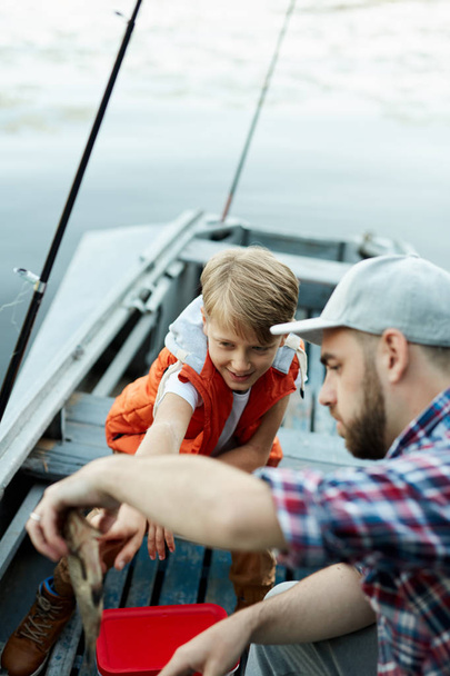 Father and son catching a fish while they fishing on the boat on the lake - Photo, Image