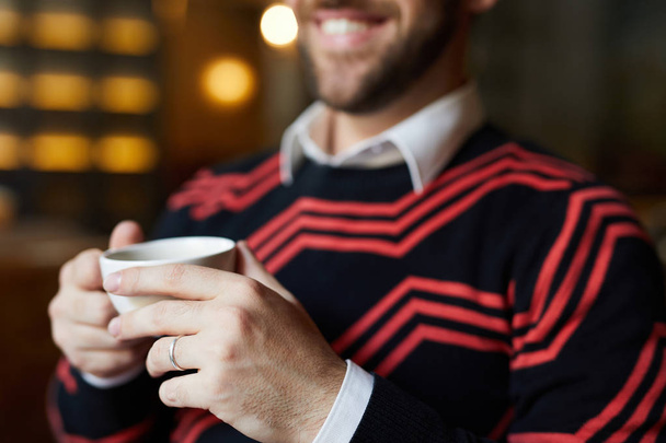 Homem contemporâneo em suéter segurando xícara de chá ou café e desfrutando de pausa no café
 - Foto, Imagem