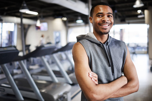 Heureux jeune sportif avec les bras croisés sur la poitrine debout par des équipements de sport dans la salle de gym d'entraînement
 - Photo, image