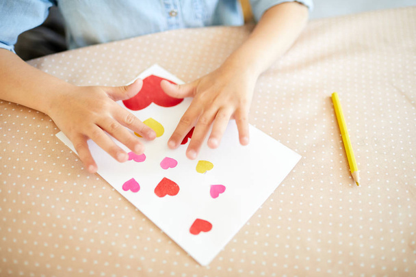 Τα χέρια του δημιουργικού μικρού κοριτσιού πάνω από χειροποίητη κάρτα με πολλές καρδιές προετοιμασμένες για τη μητέρα - Φωτογραφία, εικόνα