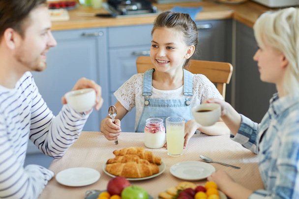 Filhinha feliz olhando para o pai enquanto toma café da manhã à mesa servida
 - Foto, Imagem