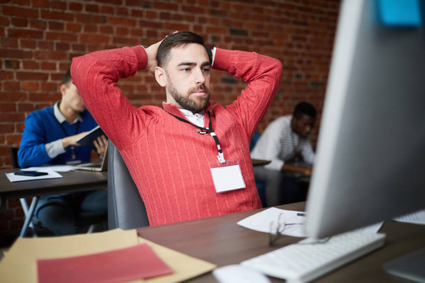 Σύγχρονος επιχειρηματίας που κάθεται μπροστά από την οθόνη του υπολογιστή και αναζητά διαδικτυακές πληροφορίες κατά τη διάρκεια της εργάσιμης ημέρας στο γραφείο - Φωτογραφία, εικόνα