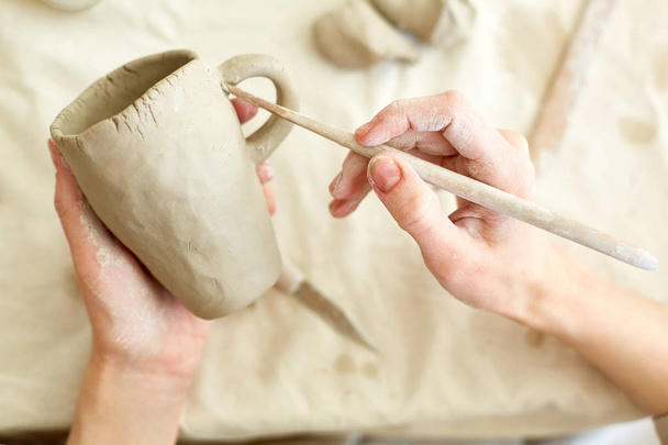 Manos de joven maestro con herramienta de mano trabajando con detalles de taza de arcilla
 - Foto, imagen