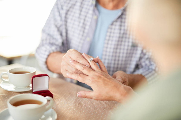 Dojrzały człowiek zakładanie jego żona palec pierścionek z brylantem zarówno siedząc przy stole i herbatę - Zdjęcie, obraz