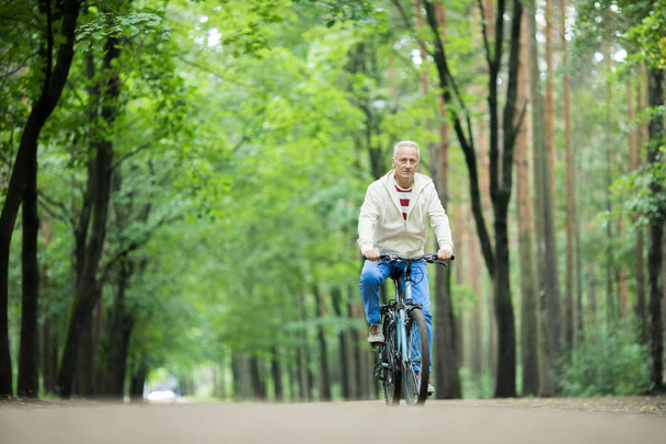 Nyugdíjas aktív férfi lovaglás kerékpár mentén erdei út között greeen fák a nyári napon - Fotó, kép