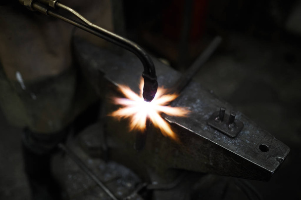 Spécialiste forgeron utilisant outil de soudage tout en travaillant sur pièce de fer sur enclume
 - Photo, image