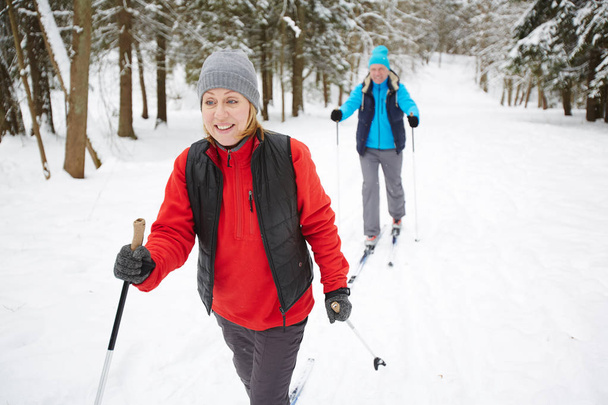 Gelukkig rijpe vrouw in sportkleding skiën met haar echtgenoot in winter forest - Foto, afbeelding