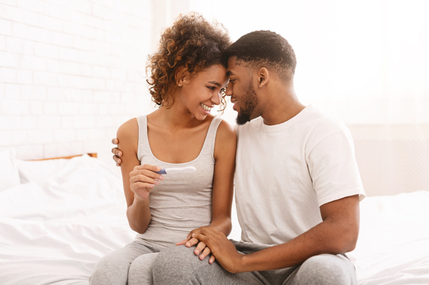 Happy couple holding positive pregnancy test on bed - Photo, Image