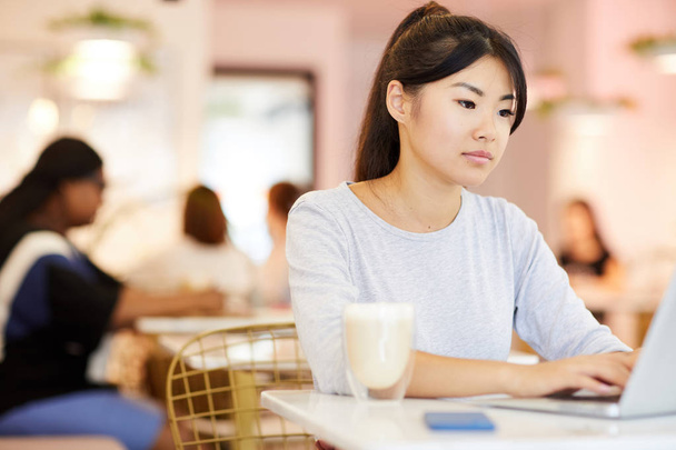 Asyalı kız dizüstü tuş takımı üzerinde yazma ve üniversiteden sonra kafede gezinirken ekranına bakarak - Fotoğraf, Görsel
