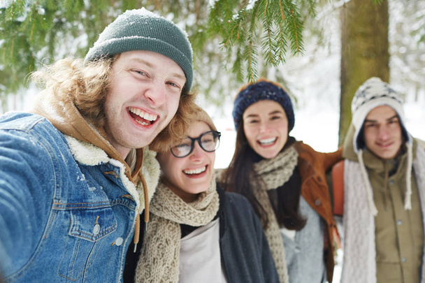 Portret czterech szczęśliwych młodych ludzi korzystających z czasu w ośrodku zimowym i śmiać się wesoło patrząc na kamerę, skupić się na człowieku z przodu - Zdjęcie, obraz