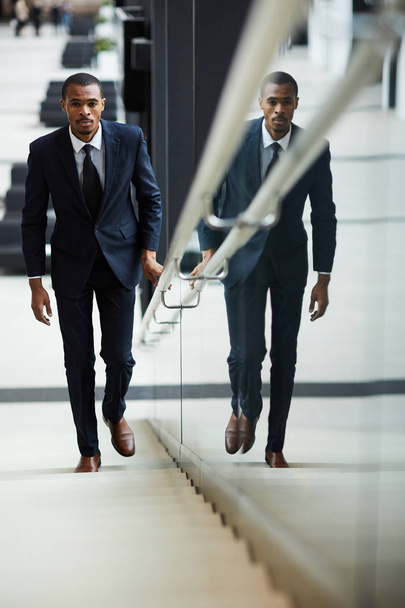 Agente afroamericano en ropa formal subiendo escaleras dentro del moderno centro de negocios
 - Foto, Imagen