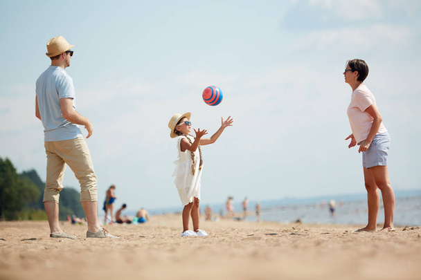 夏休みを楽しみながらビーチでボール遊びをする幸せな現代の家族の完全な長さの肖像画 - 写真・画像