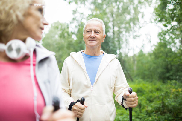 Hombre de pelo gris envejecido en ropa deportiva mirando a su esposa mientras caminaba en el parque
 - Foto, imagen