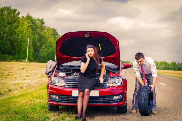 The concept of roadside assistance. A woman stands at the open hood of the car and calls. Man rolls spare tire - Φωτογραφία, εικόνα