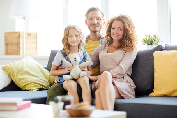 Aile evde dinlenirken yanında anne ile babası dizlerinin üzerinde oturan teddybear ile sevimli kız - Fotoğraf, Görsel