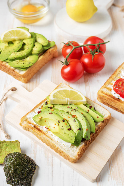 Sliced avocado on toast bread with spices on white wooden background. - Foto, afbeelding