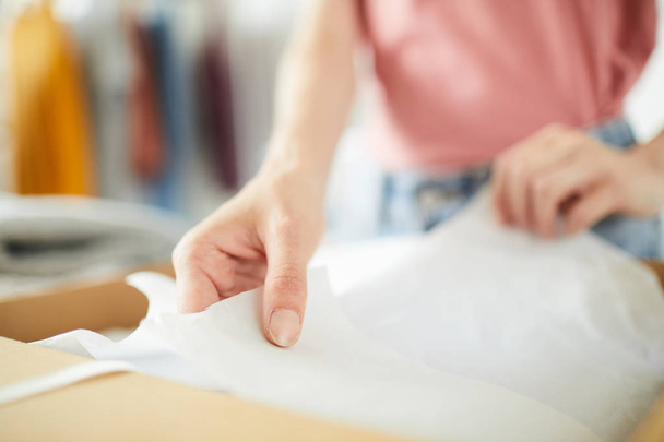 Handen van jonge nauwkeurige Designer vouwen Pack papier tijdens het inpakken van nieuw gemaakte kleren voordat ze naar de klant - Foto, afbeelding