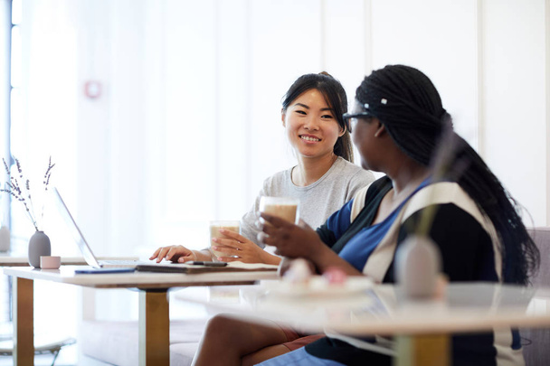 Mujeres jóvenes en ropa casual tomando bebidas mientras están sentadas en la cafetería, discutiendo momentos de trabajo y preparando la presentación
 - Foto, imagen