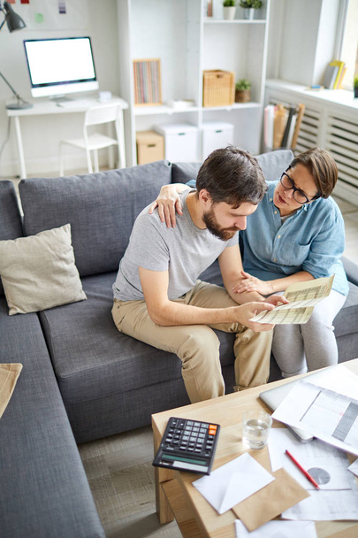 Молодой человек пытается решить финансовые проблемы, чтобы оплачивать ежемесячные счета в то время как его жена поддерживает его
 - Фото, изображение
