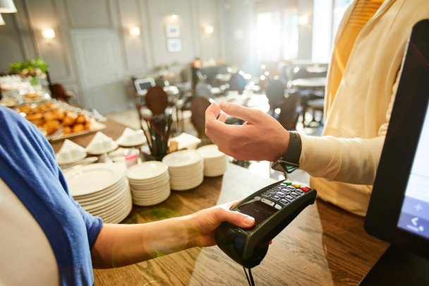 Mão de jovem com smartwatch no pulso sobre a máquina de pagamento realizada pelo assistente de café
 - Foto, Imagem