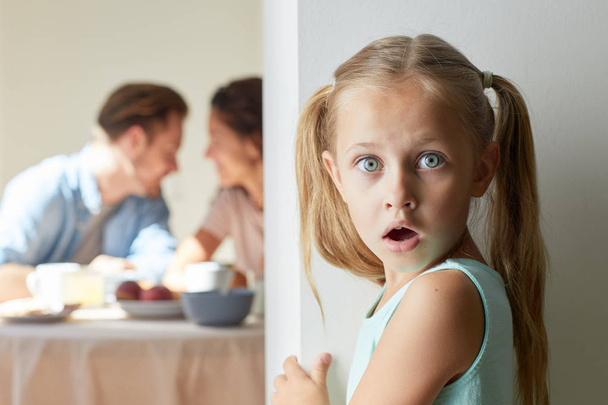 Verbaasd klein meisje hoorde het laatste nieuws tijdens haar ouders praten door het ontbijt in de keuken - Foto, afbeelding