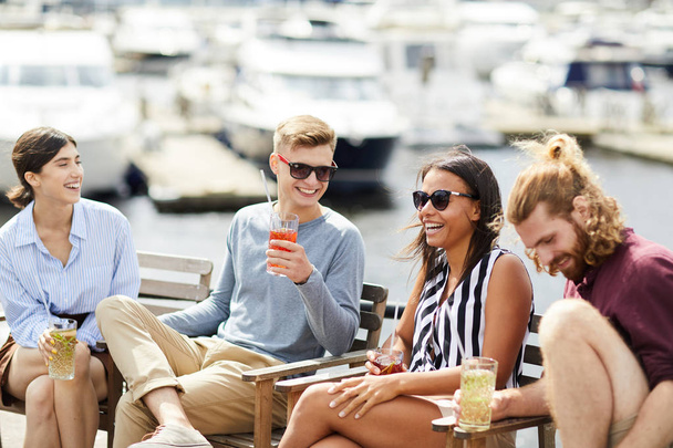 Happy young laughing people with drinks enjoying summer weekend by waterside - Fotó, kép