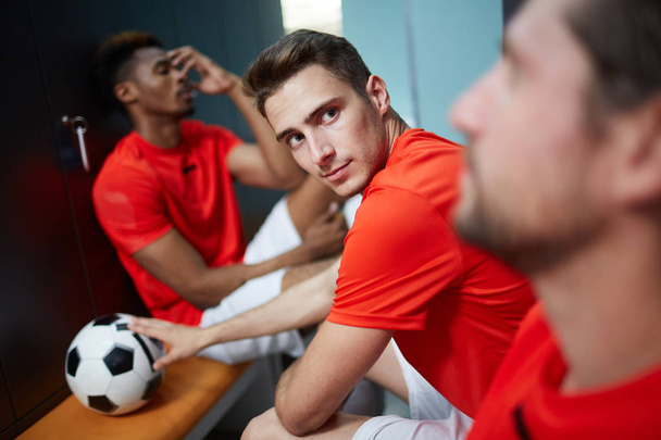 Een van de jonge voetballers kijken naar zijn partner tijdens pauze in wijzigen-kamer na wedstrijd - Foto, afbeelding