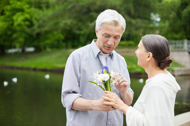 Vanhempi mies kukkakimpun kanssa puhuu valkoisista vaimolleen ulkona.
 - Valokuva, kuva