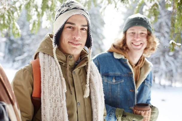 Retrato de dois jovens sorridentes posando no resort de inverno em pé na floresta nevada e olhando para a câmera
 - Foto, Imagem