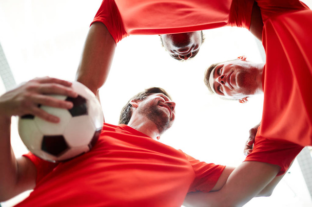 Tres jóvenes futbolistas mirándose mientras hacen un círculo de unidad
 - Foto, Imagen