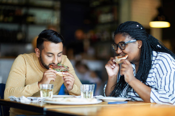 Głodny dziewczyna i facet jedzenia apetyczny pizzy z boczkiem w kawiarni lub restauracji w porze lunchu - Zdjęcie, obraz