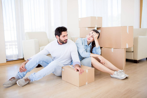 junges Paar ruht sich auf dem Boden seines neuen Hauses bei einem Stapel Kisten aus - Foto, Bild
