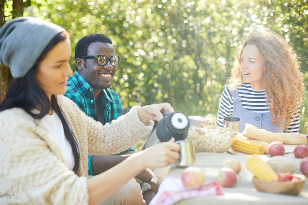 Tizenéves lány ömlött a tea a szabadban ebéd vele interkulturális barátok mellett ülő - Fotó, kép