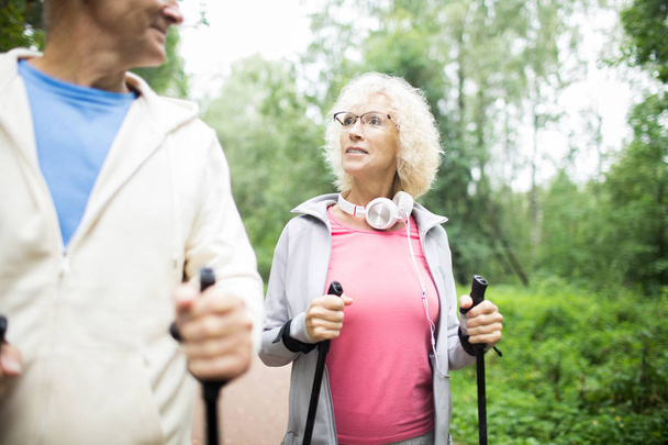 Aktywna Starsza blondynka w okularach i SPORTWEAR Trekking z mężem w letni dzień - Zdjęcie, obraz