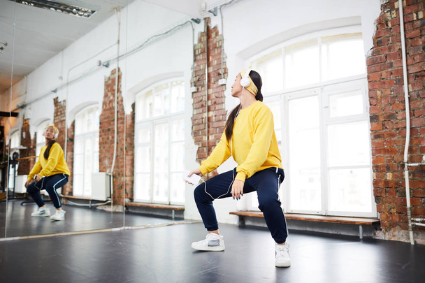 Active girl with headphones and smartphone learning hip hop dance in front of mirror in studio - Photo, Image